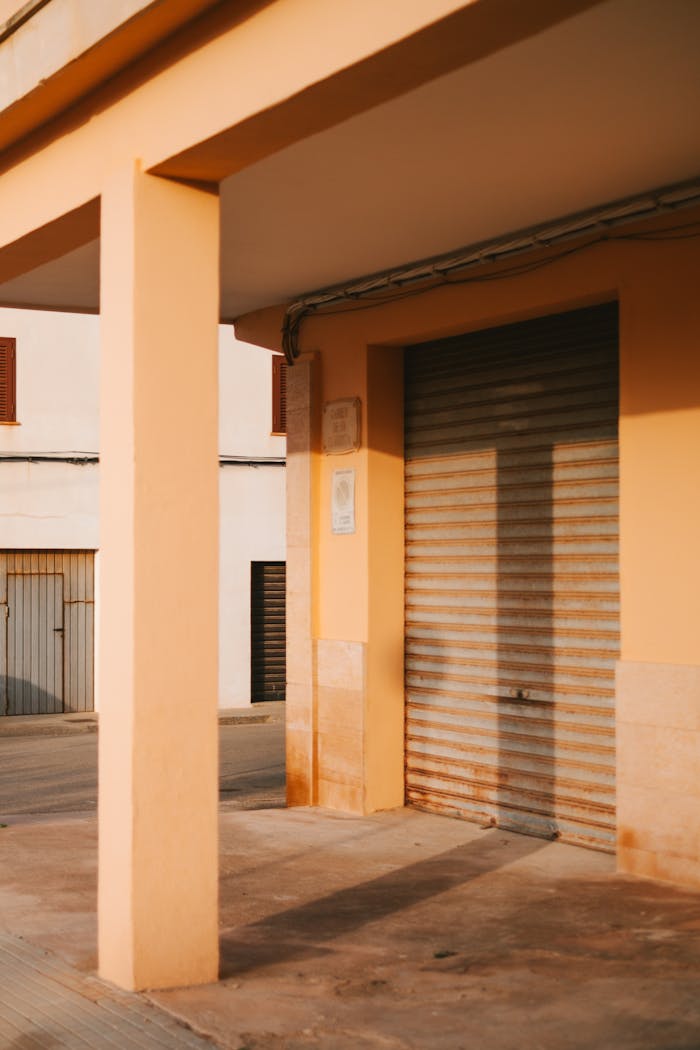 Sunlit building entrance with garage door in Sa Ràpita, Spain.